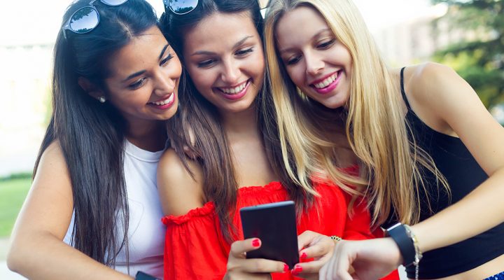 Outdoor portrait of three girls chatting with their smartphones at the park.